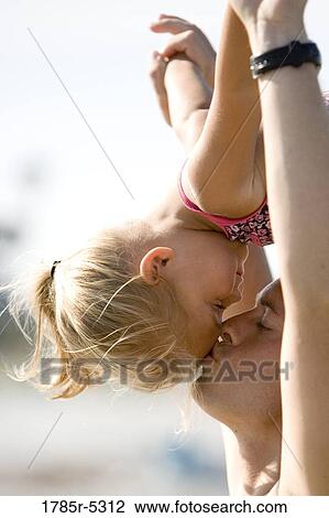 Stock Image - Young father kissing daughter on forehead. Fotosearch