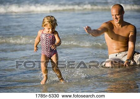Young father sitting in the waves while his daughter playfully runs away from him View Large Photo Image Stock Image - Young father sitting in the waves while his daughter playfully runs away from him. Fotosearch