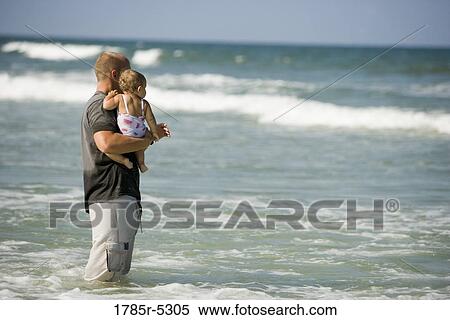 Young father with baby daughter standing on beach looking out towards the ocean View Large Photo Image Stock Photography - Young father with baby daughter standing on beach looking out towards the ocean. Fotosearch