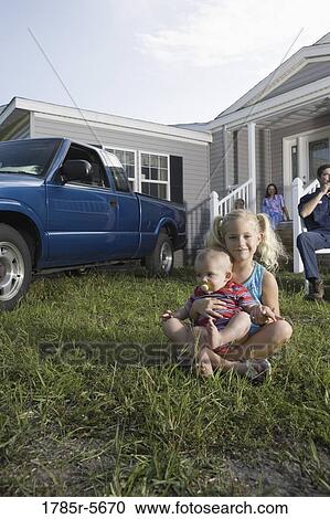 Young girl and a baby sitting on the front lawn of a trailer home, family in background View Large Photo Image Stock Image - Young girl and a baby sitting on the front lawn of a trailer home, family in background. Fotosearch