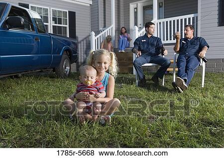 Young girl and a baby sitting on the front lawn of a trailer home, family in background View Large Photo Image Stock Photo - Young girl and a baby sitting on the front lawn of a trailer home, family in background. Fotosearch
