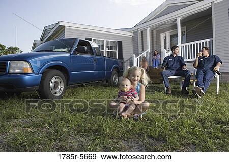 Young girl and a baby sitting on the front lawn of a trailer home, family in background View Large Photo Image Stock Photo - Young girl and a baby sitting on the front lawn of a trailer home, family in background. Fotosearch