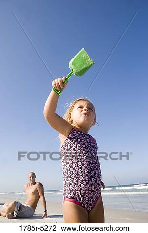 Stock Image - Young girl at the beach with father watching in background. Fotosearch