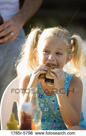 Young girl eating a burger View Large Photo Image Stock Photo - Young girl eating a burger. Fotosearch