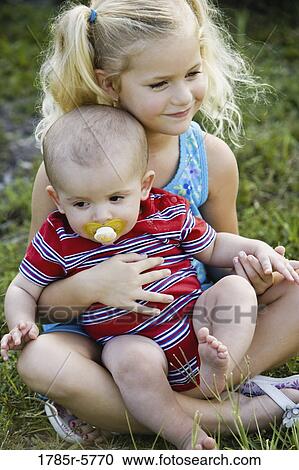 Young girl holding a baby sitting on grass View Large Photo Image Stock Image - Young girl holding a baby sitting on grass. Fotosearch