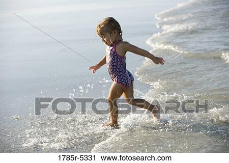 Stock Image - Young girl playing on beach, running into the surf. Fotosearch