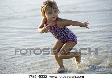 Stock Image - Young girl playing on beach, running into the surf. Fotosearch