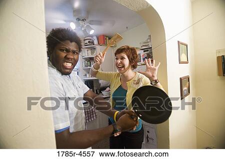 Stock Photo - Young inter-racial couple goofing around with frying pan. Fotosearch