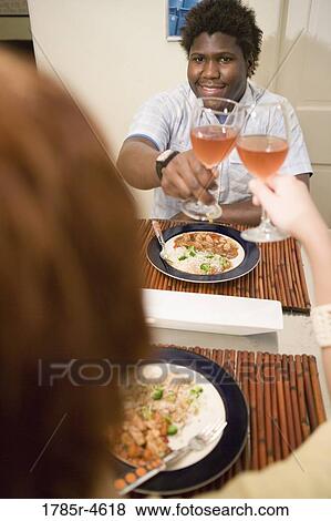 Stock Photo - Young inter-racial couple sitting at dining table toasting with glasses of wine. Fotosearch