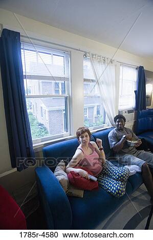 Young inter-racial couple sitting on sofa eating popcorn View Large Photo Image Stock Image - Young inter-racial couple sitting on sofa eating popcorn. Fotosearch