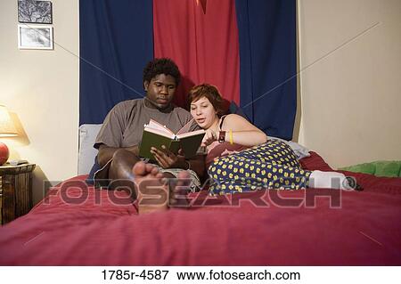 Stock Photo - Young interracial couple reading a book together on a bed. Fotosearch