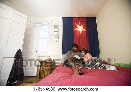 Stock Photograph - Young interracial couple reading a book together on a bed. Fotosearch