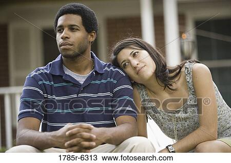 Stock Image - Young interracial couple sitting in front of house. Fotosearch