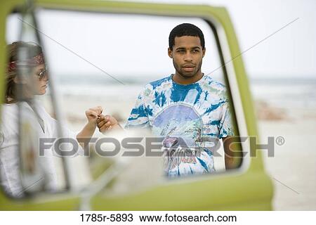 Young man and young woman standing by vehicle at beach View Large Photo Image Stock Image - Young man and young woman standing by vehicle at beach. Fotosearch