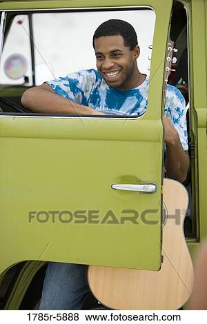 Stock Photo - Young man holding guitar sitting in van. Fotosearch
