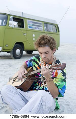 Young man in hippie fashion playing guitar by van at beach View Large Photo Image Picture - Young man in hippie fashion playing guitar by van at beach. Fotosearch
