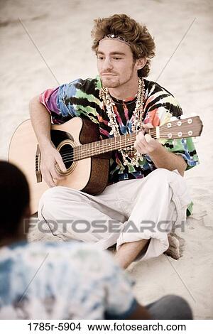 Young man in hippie fashion playing guitar at beach View Large Photo Image Picture - Young man in hippie fashion playing guitar at beach. Fotosearch