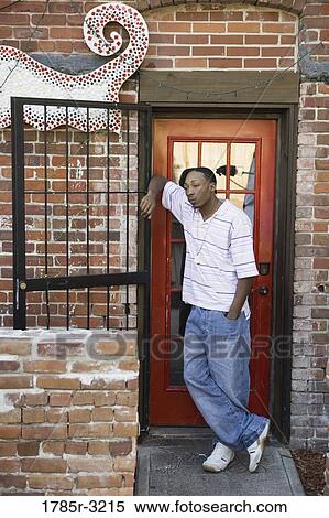 Stock Photography - Young man leaning against dilapidated door in back alley. Fotosearch