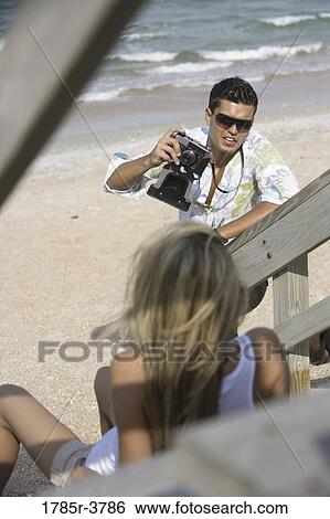 Stock Photograph - Young man photographing a young woman at the beach. Fotosearch