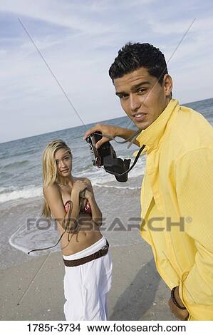 Picture - Young man photographing scantily clad woman on the beach. Fotosearch