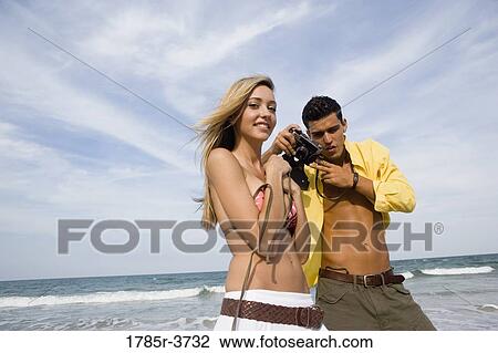 Young man photographing scantily clad woman on the beach View Large Photo Image Stock Image - Young man photographing scantily clad woman on the beach. Fotosearch