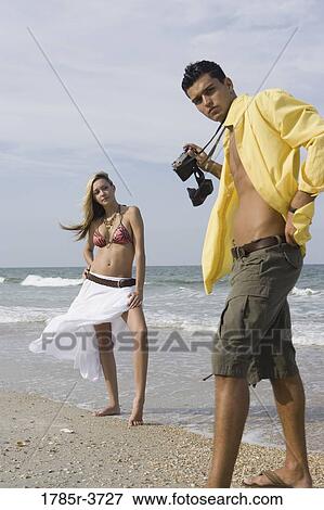 Stock Photo - Young man photographing scantily clad woman on the beach. Fotosearch