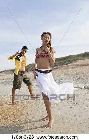 Young man photographing scantily clad woman on the beach View Large Photo Image Stock Photo - Young man photographing scantily clad woman on the beach. Fotosearch