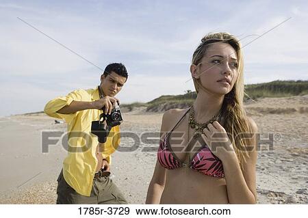 Stock Photo - Young man photographing scantily clad woman on the beach. Fotosearch