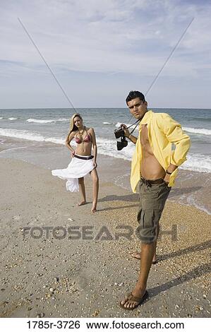 Young man photographing scantily clad woman on the beach View Large Photo Image Stock Photograph - Young man photographing scantily clad woman on the beach. Fotosearch