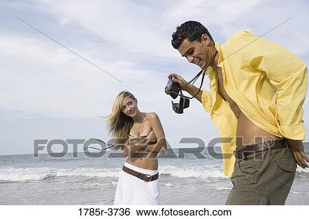 Young man photographing scantily clad woman on the beach View Large Photo Image Stock Photograph - Young man photographing scantily clad woman on the beach. Fotosearch