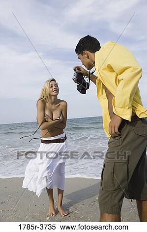 Stock Photography - Young man photographing scantily clad woman on the beach. Fotosearch
