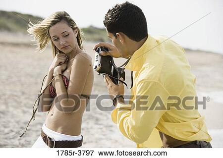 Young man photographing woman undressing at the beach View Large Photo Image Stock Photo - Young man photographing woman undressing at the beach. Fotosearch