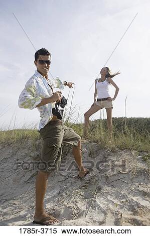 Stock Photography - Young man pointing at a young woman at the beach. Fotosearch