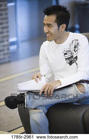 Stock Image - Young man sitting on the sofa with a book. Fotosearch