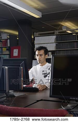 Young man using a computer in the library View Large Photo Image Stock Photo - Young man using a computer in the library. Fotosearch
