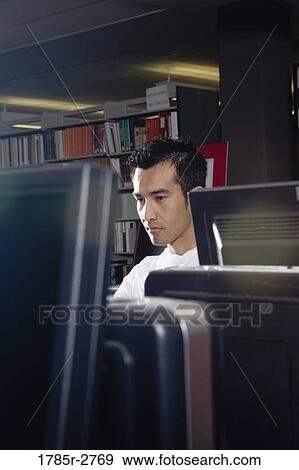 Stock Photo - Young man using a computer in the library. Fotosearch