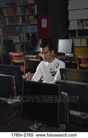 Young man using a computer in the library View Large Photo Image Stock Photography - Young man using a computer in the library. Fotosearch