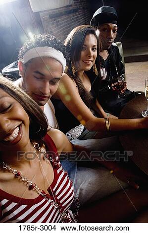 Picture - Young men and women in hip-hop fashion partying at a bar. Fotosearch