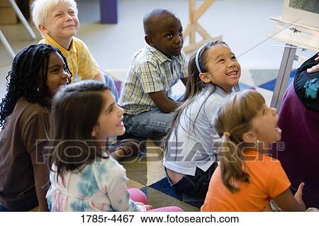 Young students seated on floor watching and listening attentively View Large Photo Image Stock Photo - Young students seated on floor watching and listening attentively. Fotosearch