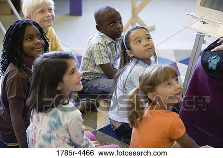 Young students seated on floor watching and listening attentively View Large Photo Image Stock Photograph - Young students seated on floor watching and listening attentively. Fotosearch