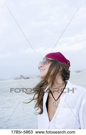 Stock Image - Young woman in hippie fashion smiling against sky at beach. Fotosearch