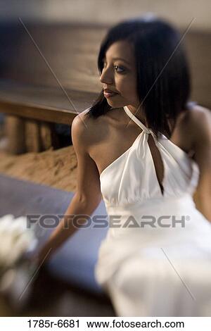Stock Image - Young woman in white gown holding a white bouquet. Fotosearch