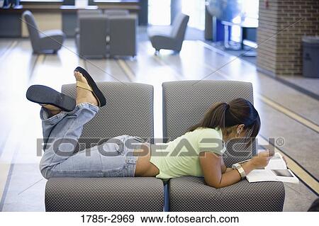 Stock Photo - Young woman lying on the sofa reading a book. Fotosearch
