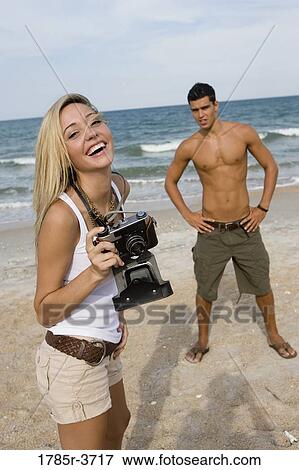 Stock Photo - Young woman photographing a man at the beach. Fotosearch