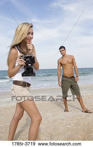 Stock Photo - Young woman photographing a man at the beach. Fotosearch