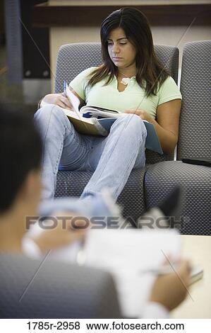 Stock Photo - Young woman reading a book while sitting on a sofa. Fotosearch