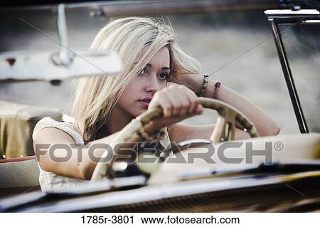 Stock Image - Young woman sitting in antique convertible car. Fotosearch