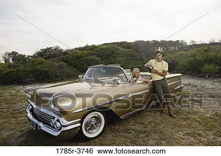 Young woman sitting in antique convertible car while man stands against the door View Large Photo Image Stock Photograph - Young woman sitting in antique convertible car while man stands against the door. Fotosearch
