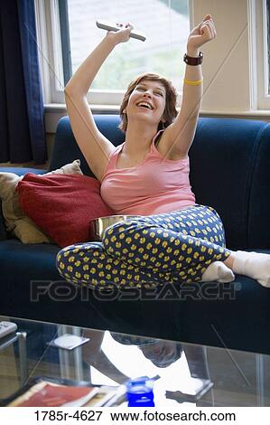 Stock Photo - Young woman sitting on a sofa cheering. Fotosearch