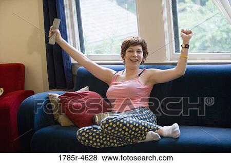 Stock Photo - Young woman sitting on a sofa cheering. Fotosearch